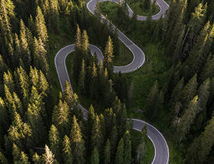 A curving road is seen from above, winding through a forest